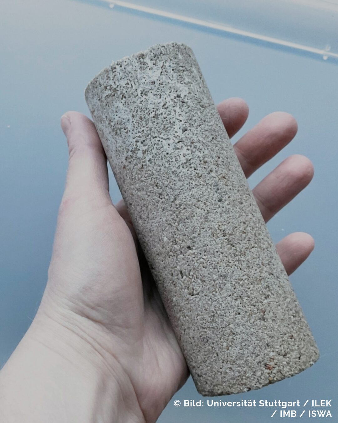 Eine Hand hält ein zylinderförmiges Stück Beton